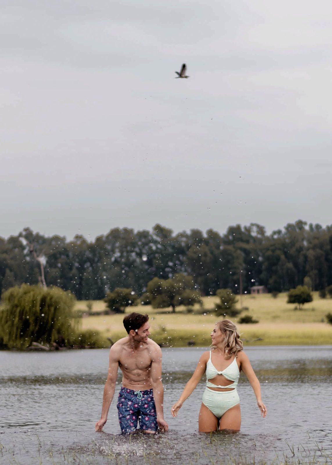 Couple walking through a lake beneath a flying bird